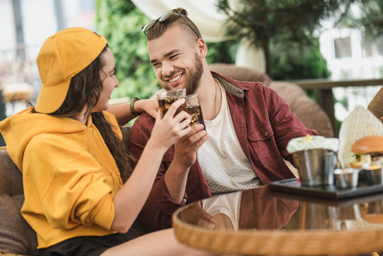 Young couple in love having fun spending leisure time together at restaurant, eating burgers and french fries, drinking cola 
