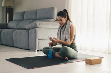 Fit woman smiling and using smartphone on yoga mat