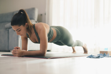 Slim woman doing plank exercise on mat at home