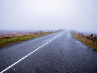 Asphalt road and fields in country side in a fog. Dangerous driving conditions with low visibility and wet road surface. Mist over wild nature.