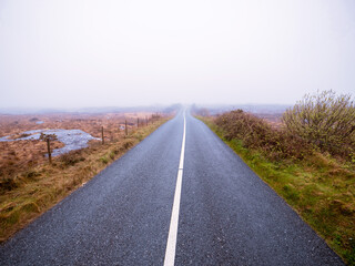 Asphalt road and fields in country side in a fog. Dangerous driving conditions with low visibility and wet road surface. Mist over wild nature. Irish country side.