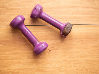Two light small purple color dumbbell on a wooden floor. One has serious damage to plastic surface. Hard fitness workout concept. Old equipment to get into great physical form.