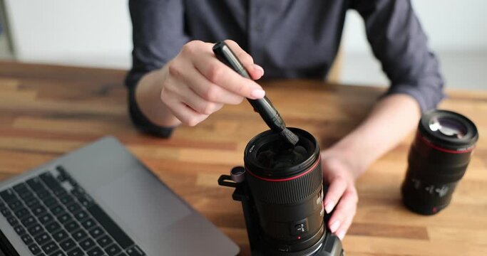 Woman is cleaning camera lens with special brush closeup. Care of optics concept