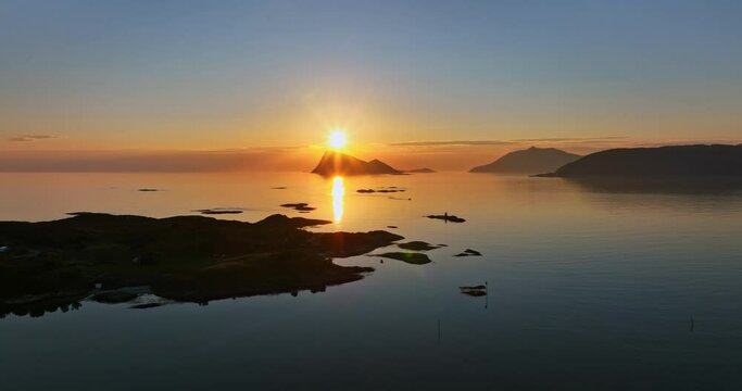 Aerial tracking shot of arctic isles,with the midnight sun sunburst in the background