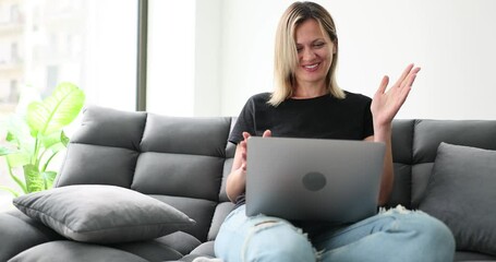 Smiling young woman using laptop, sitting on sofa at home, chatting on video call. Pretty girl chatting online in social network