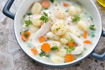 Creamy soup with chicken fillet and potato gnocchi in a grey serving pan, middle close-up, horizontal shot, selective focus