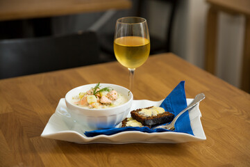 A bowl of Finnish Lohikeitto soup served on wooden table with a piece of Swedish rye bread. Creamy broth, tender potatoes, and flaky pink salmon create a delicious dish, with white wine 