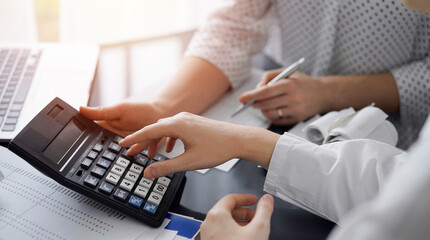 Woman accountant using a calculator and laptop computer while counting taxes for a client. Business...