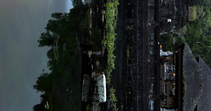 Vertical slow motion static shot of a pond in the sacred pura tirta empul temple with view of the temple buildings, flying birds and water plants in ubud on bali indonesia