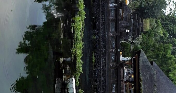 Vertical Slow motion static shot of a pond in the legendary pura tirta empul temple overlooking the temple buildings, flying birds and water plants in ubud on bali indonesia