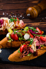 Italian food bruschetta with beef slices, capers, cherry tomatoes, mozzarella, salmon, cucumber, lettuce.