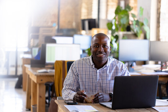 Portrait of happy african american casual businessman using laptop and having lunch in office