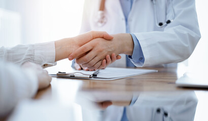 Doctor and patient shaking hands above the wooden table in clinic. Medicine concept