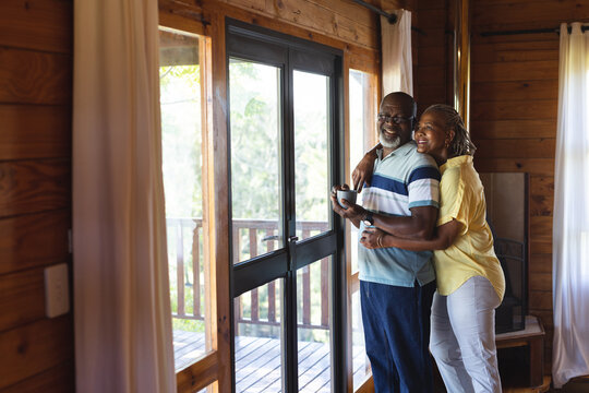 Happy senior african american couple embracing and looking out window at home