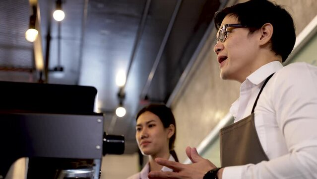 Head trainer of barista school standing in front of coffee machine explains or demonstrates to student trainee or entrepreneurship small business in classroom, Asian manager or chief teaching staff