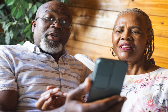 Senior african american couple sitting on sofa and using smartphone at home