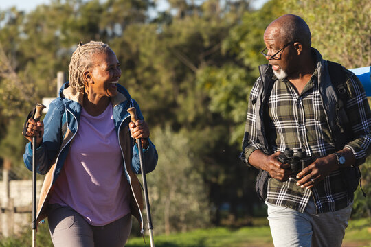 Happy Senior African American Couple With Backpacks Walking In Sunny Nature