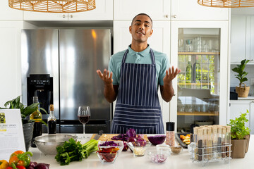 Happy biracial male cooking vlogger in apron talking in sunny kitchen