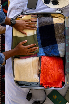 Hands of biracial man packing suitcase in sunny bedroom, copy space