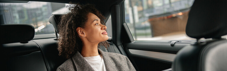 Woman freelancer working on laptop sitting on car backseat on way to office and looking at window