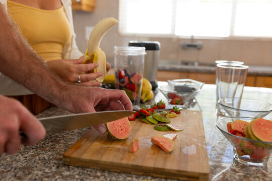 Hands of caucasian couple preparing and chopping fruits in kitchen