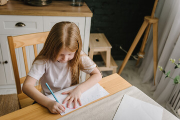 A little girl draws a picture with pencils at home. Child painting a picture with school supplies. Preschool kid drawing and doing homework. Top view.