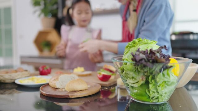 Close up vegetables salad in glessed bowl. Focus shot of vegetables salad in glessed bowl and mother and daughter helping together making sandwiches on blurred background. Healthy food concept