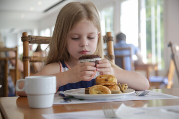 Cute 5 years old girl eating chocolate muffin at the restaurant	
