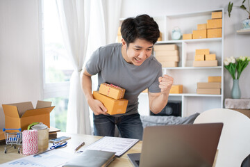 Happy man Celebrating Order from Internet Customer: New Business Style at Home, Online Selling, Young Entrepreneur's Success: Work-from-Home SME Owner Thrives in Online Sales, Packing Box.