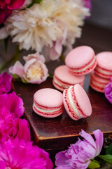 Pink macaroons lie on a wooden box surrounded by peony flowers