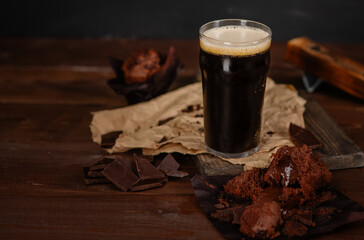 Glass of beer stout standing on wooden board with chocolate muffin