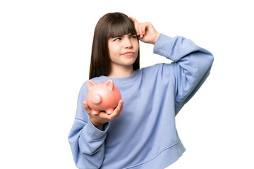 Little girl holding a piggybank over isolated chroma key background having doubts and with confuse...