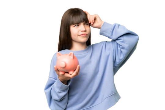 Little girl holding a piggybank over isolated chroma key background having doubts and with confuse face expression