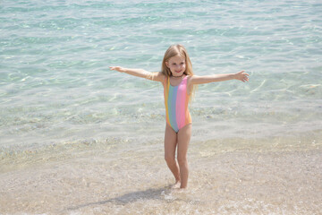 Fototapeta na wymiar Cheerful little girl playing and jumping on the sand beach
