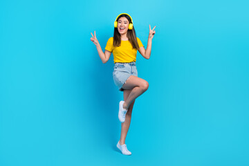 Full size photo of pretty excited girl demonstrate v-sign enjoy listen music isolated on blue color background