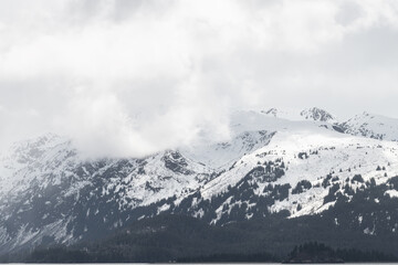 Fototapeta na wymiar Sun and shadows on a snow covered mountain with clouds and mist near Homer Alaska, USA