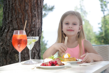 Cheerful little girl eating cake at the outdoor cafe