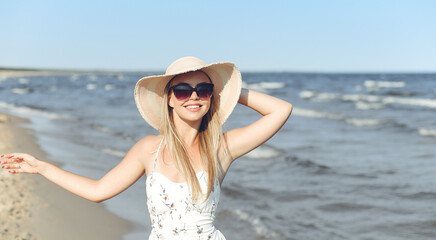 Happy blonde woman in free happiness bliss on ocean beach standing with sun glasses and hat