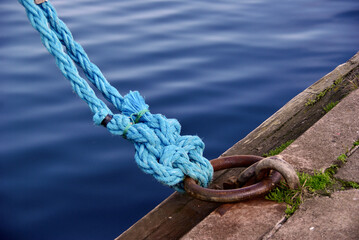 Two blue ropes with a lot of knots around a mooring ring in a harbor.