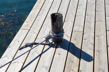 Fototapeta premium Wooden pier with a wooden pole bollard and tied ropes.