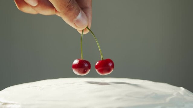 A hand puts two fused red cherries on a white cake close-up