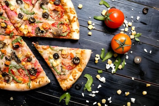 Top view of pizza on wooden table, two tomatoes lying next to it