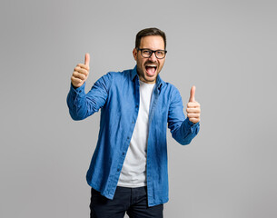 Portrait of excited happy businessman showing thumbs up sign and screaming over gray background