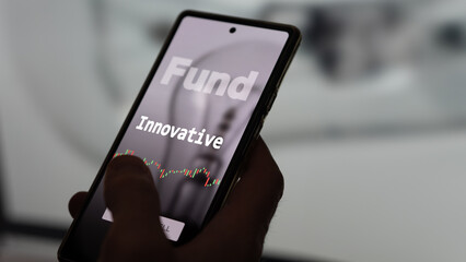 An investor's analyzing the innovative etf fund on a screen. A phone shows the prices of innovative fund.