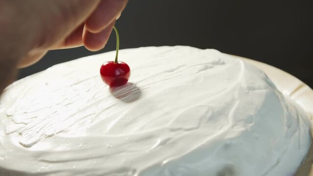 Cherry on the cake. Apotheosis. Finish. A hand puts a red cherry on a homemade white cake that rotates at an angle