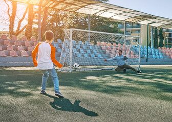 Father and Son play football on stadium outdoors, Happy family bonding, fun, players in soccer in dynamic action playing in sunny day, holidays time.
