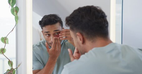 Biracial man looking in mirror applying under eye masks in bathroom, slow motion - Powered by Adobe
