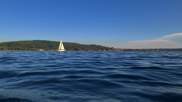 Slow-motion and low-angle view of small boat sailing in calm open lake waters of Maggiore lake in Italy. Zoom-in