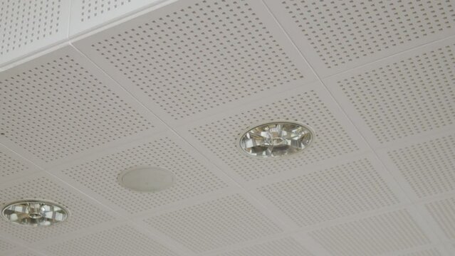 White cassette ceiling with visible small openings, recessed ceiling lights. Modern ceiling design.