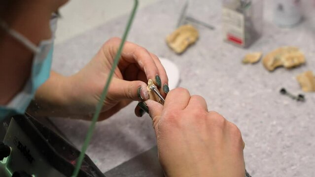 Carving out and refining an artificial tooth implant by masked dental worker in small healthcare clinic at the work-shop
